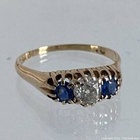 Front three-quarter view showing central diamond and flanking sapphires in yellow gold setting