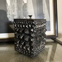 Front view of Brutalist bronze lidded vessel showing textured triangular pattern and lid with knob on top.