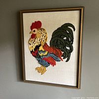 Framed crewel embroidery of a colorful rooster on cotton fabric, showing the full artwork.
