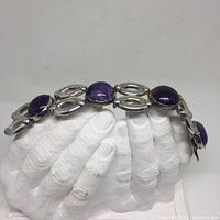 Bracelet draped over white hand-shaped display showing profile of links and stones
