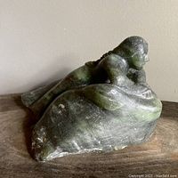 Angled front view showing figure leaning on base rock