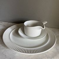 White ceramic Johnson Bros. Athena set showing gravy boat, saucer, and 12 inch round platter stacked together on marble surface.