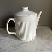 Side view of white ribbed ceramic tea pot showing handle, spout, and lid.
