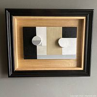 Front view of the assemblage relief painting mounted in a black and natural wood shadow box frame, showing the geometric abstract design and two circular relief elements.