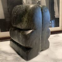 Side view of one soap stone carved bookend showing rounded, abstract Inuit style form with smooth surface and green-gray color.