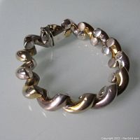Full view of bracelet showing curved polished silver links with gold tone underneath.