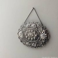 Front of the mirror showing the intricate hand chased repousse silver frame with floral designs and scalloped borders. Hanging chain attached.