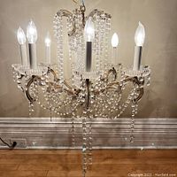 Front view of six-light crystal chandelier with lit bulbs and crystal bead draping on brass frame.