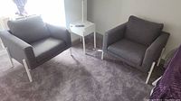 Pair of grey upholstered armchairs positioned side by side on a grey carpet in a room with natural light