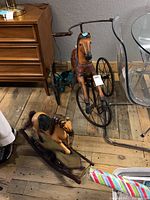Overview of both the large horse tricycle and the small rocking horse on a wooden floor between furniture pieces.