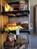Wide view showing shelves with a yellow VW Beetle model car, orange vintage car model, wooden blocks, bronze baby shoes, and an assortment of small toys on black shelving unit.