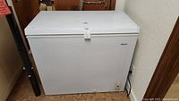 White Haier chest freezer viewed from the front showing the closed lid and the Haier logo on the upper right.
