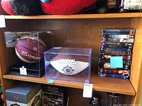 Overall shot of shelf with two collectible footballs in cases and a stack of DVD boxed sets on the right.