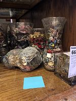 Wide view of six glass containers filled with assorted colorful costume jewelry placed on a wooden shelf.