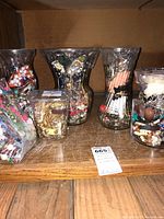 Six clear containers filled with assorted costume jewelry on a wooden surface.