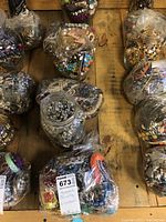 Photo of six containers wrapped in plastic containing assorted costume jewelry including beads, necklaces, bracelets, and pins