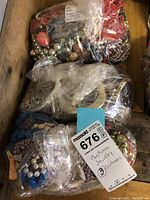 Top down photo showing three large plastic-wrapped containers filled with assorted costume jewelry including beads and faux pearls