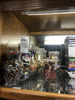 Wide shot showing six clear glass containers filled with assorted costume jewelry items including bracelets, necklaces, and earrings.