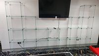 Front view of modular glass shelving with 21 cubes, clear glass connected by metal corners, staggered configuration under mounted TV.