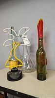 Photo showing the bottles and neon palm tree light together, arranged on a table against a gray wall.