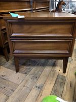 Front view of the nightstand showing the two drawers and tapered legs on wooden floor.