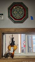 Photo showing Ambar colored glass swag lamp hanging with coiled chain and Aztec calendar wall art mounted above wooden window frame.