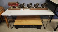 Full view of white low table with chrome legs, small cabinet underneath, placed against a wall with figurines on top