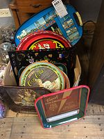 Photo shows multiple vintage tin trays in a box including Coca-Cola, beer, and floral design trays.