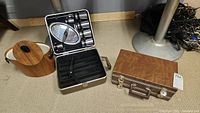Closed metal case with latch and handle for Trav-L-Bar portable bar set next to a wood-grain patterned ice bucket with cream handles.