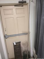 Photo of closed door with metal sluice box leaning against it and part of shelving unit visible