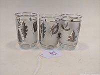 Photo showing three clear glass tumblers decorated with silver foliage patterns from a frontal angle to display design details.