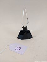 Perfume bottle showing front with black geometric base and clear faceted stopper, angled slightly left.