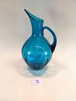 Front angle view of the teal blown glass pitcher showing its shape and handle.