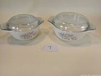 Pair of Pyrex Blue Iris pattern casserole dishes with lids, shown side by side to illustrate size difference and matching design.