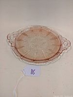 Front view of the round pink depression glass sandwich tray with cherry blossom pattern and handles.
