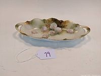 Angled side view of the oblong porcelain dish showing white roses decoration and decorative handles.