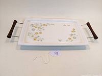 Top view of the rectangular white enamel tray with floral bouquet pattern and wooden handled wire base shown horizontally.