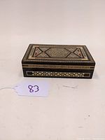 Front view of rectangular wooden box with detailed bone inlay on the lid, showing geometric and floral motifs.