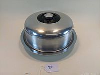 Vintage aluminum cake stand with dome cover shown from a slight angle with the knob visible on top.