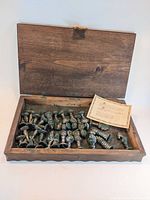 Wooden box open showing silver and gold plated chess pieces loosely placed inside, and a certificate card on top.