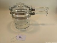 Pyrex Flameware double boiler set stacked together showing the two pots and the lid on top with clear glass handles and knob.