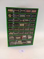 Front view of the green Raaco storage cabinet showing all 35 clear plastic drawers, some drawers tied with string, containing various sewing threads and notions.