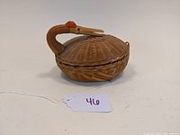 Side view of the handwoven wicker swan shaped basket featuring a covered lid and red accent on the swan's head.