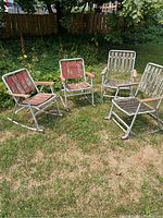 Four mismatched mid century aluminum rocking lawn chairs placed on grass, showing two with red slats and two with greenish/natural metal slats, all with aluminum frames and wooden armrests.