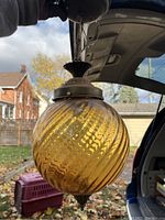 Photo of one amber glass globe light fixture suspended outdoors, showing ribbed design and metal top and bottom fixtures.
