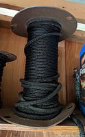 Photo showing a partial roll of braided black rope wound on a spool with metal or wooden end plates.
