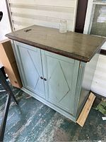 Front view of wooden cabinet with distressed green painted doors and scratched top surface