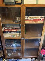 Photo showing the full front view of the vintage wooden cabinet with glass doors and various board games inside (not included).