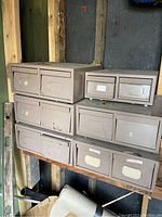 Photo of various sizes of brown metal file drawers stacked on a shelf against a wall with visible labels on the drawers.