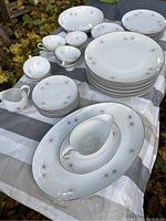 Set of white porcelain dishes arranged on cloth, showing large and smaller plates, cups, saucers, creamer, and gravy boat with atomic starburst pattern and gold accents.